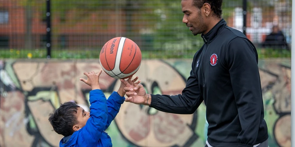 A child reaches for a basketball beside a coach at Orchardson Avenue’s outdoor court in Belgrave.
