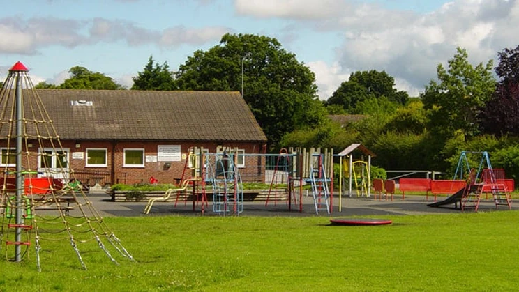 Climbing equipment, swings and a slide on grass beside Chineham Village Hall
