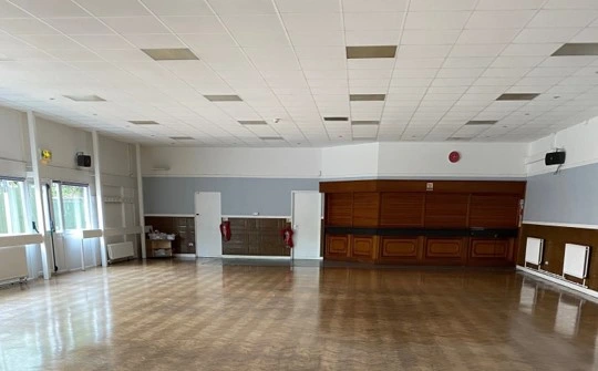 Empty main hall at Fryerns Community Centre, with a wooden floor, windows and a closed serving bar.