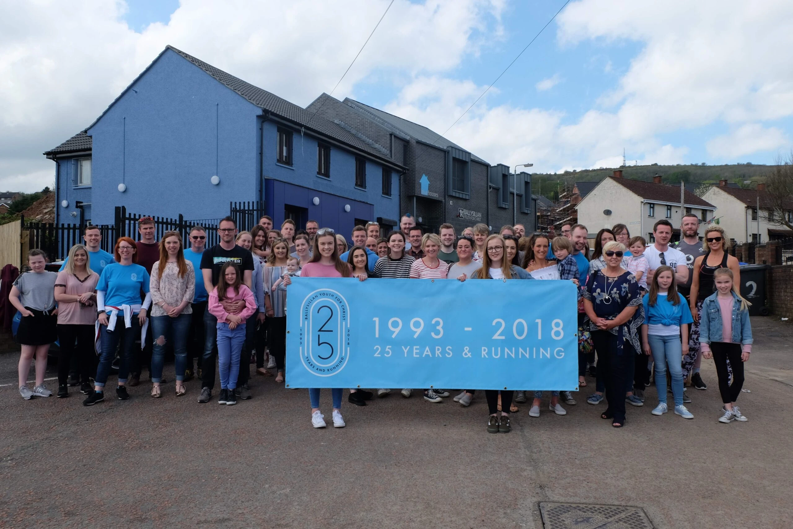 Community group outside the BlueHouses with a 1993–2018 anniversary banner