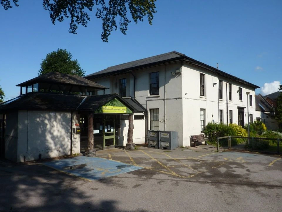 White-painted Sherwood Community Centre with its entrance, windows and forecourt beneath trees.