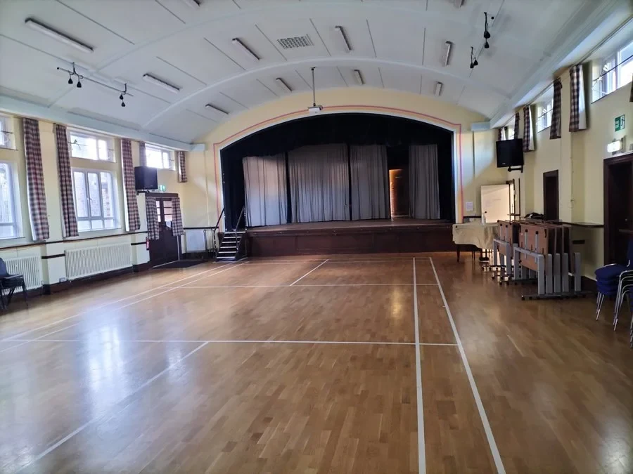 Wooden floor, tall windows and a curtained stage inside St Peter’s main hall in Henleaze