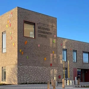 Brick exterior of Meadows Community Centre with colourful climbing holds and its name on the wall