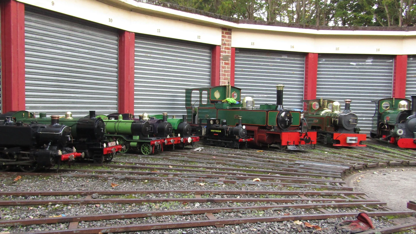Miniature steam locomotives lined up on tracks outside the engine sheds at Mizens Railway