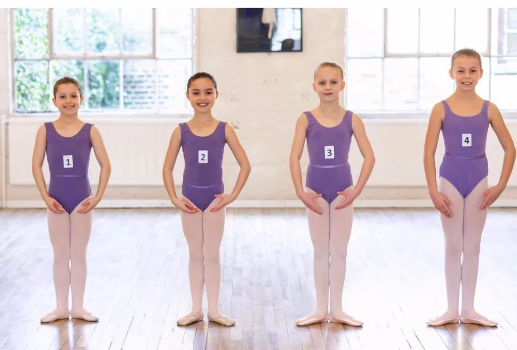 Four young ballet dancers in purple leotards standing in a bright hall, in a photograph from Joanne Ward Dance Academy