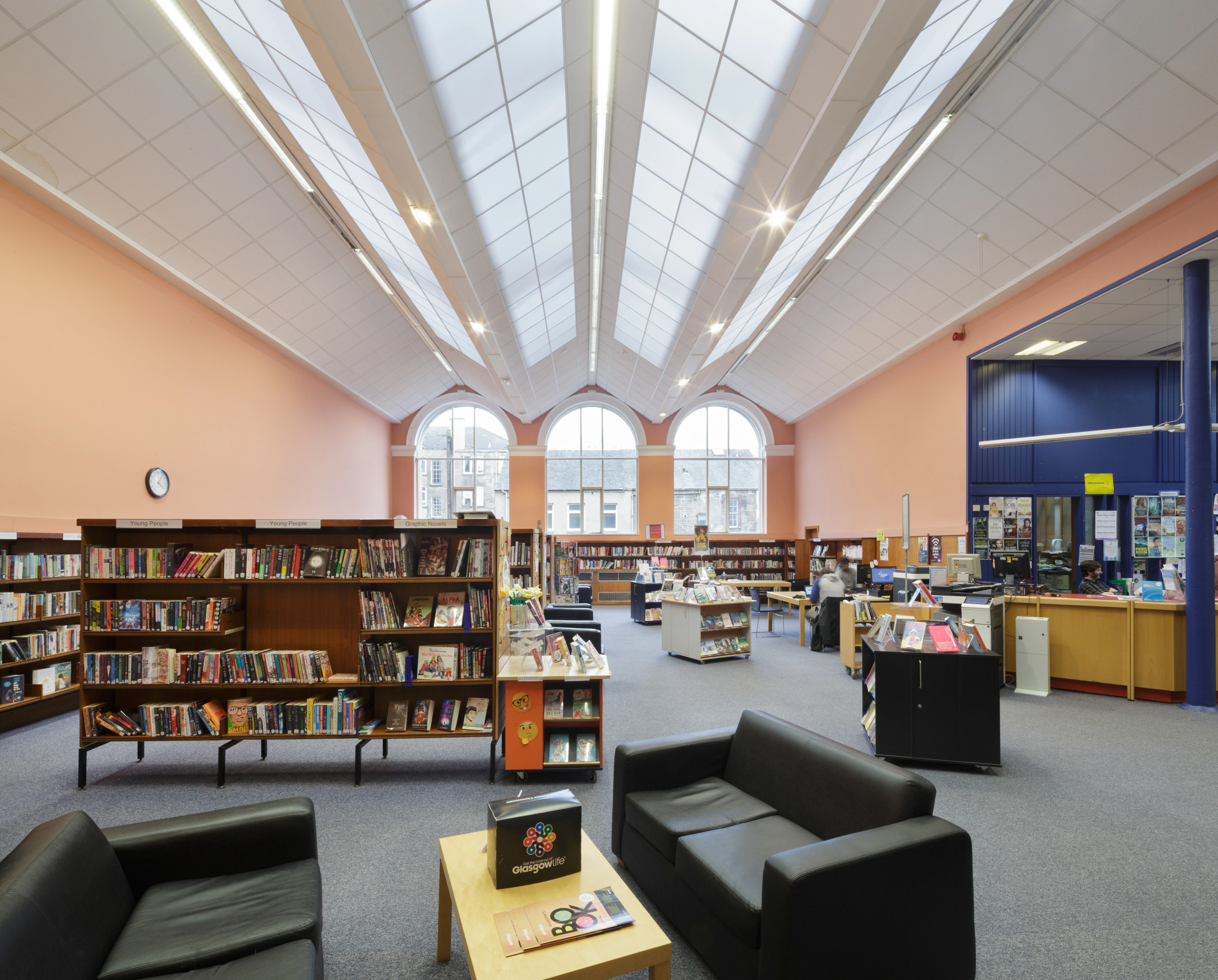 Bookshelves and black seating beneath the skylit ceiling and arched windows of Dennistoun Library
