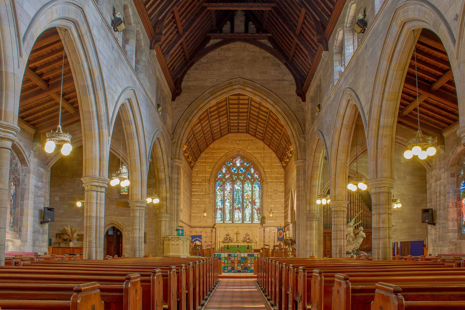 Stone arches and wooden pews face a stained-glass window inside All Hallows, Allerton.