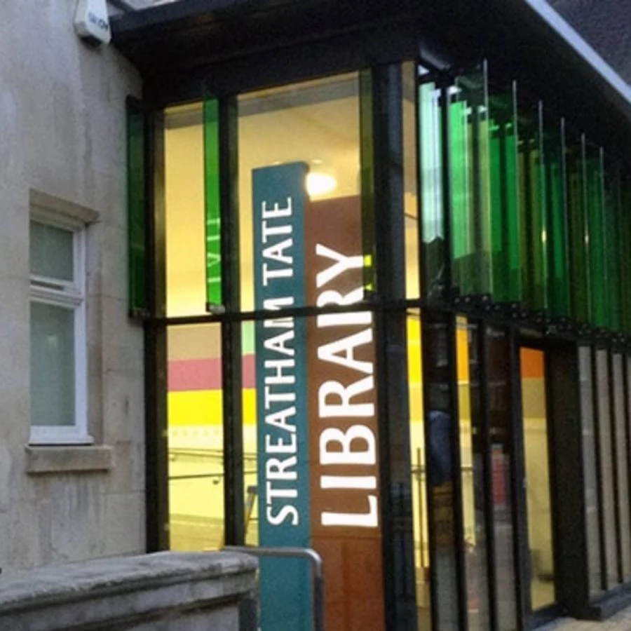 Glass entrance to Streatham Tate Library with a tall library sign and green window fins