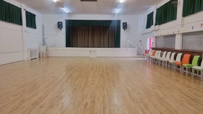 Empty wooden-floor main hall with a stage and chairs at Leigh Park Centre