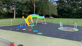 Green and yellow play equipment and an inclusive roundabout on dark play surfacing at Locks Heath House Park