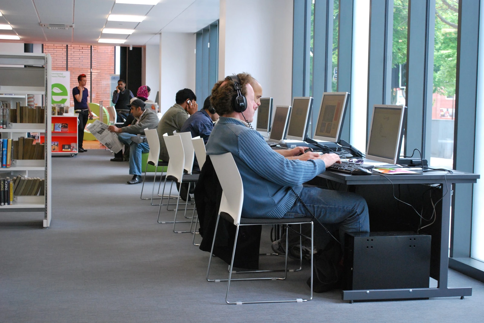 Visitors using computers beside the windows inside Longsight Library and Learning Centre.