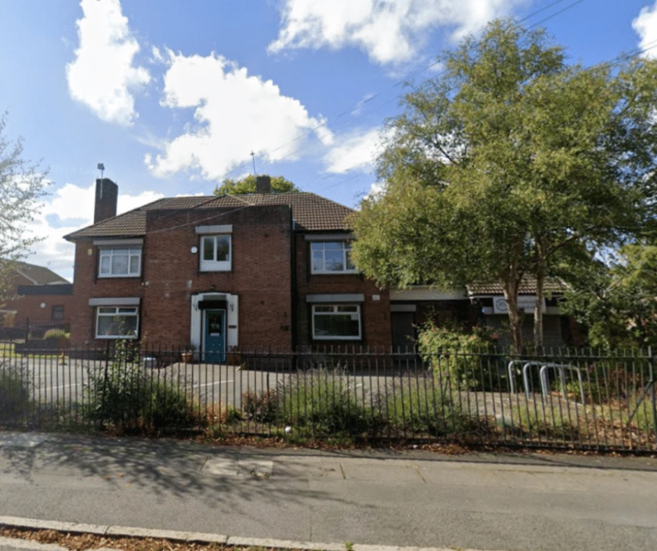 Brick frontage of Triple C’s community building on Sedgemoor Road, with railings and a leafy tree.