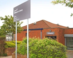 Whiterock Library’s red-brick exterior, entrance sign and leafy shrubs