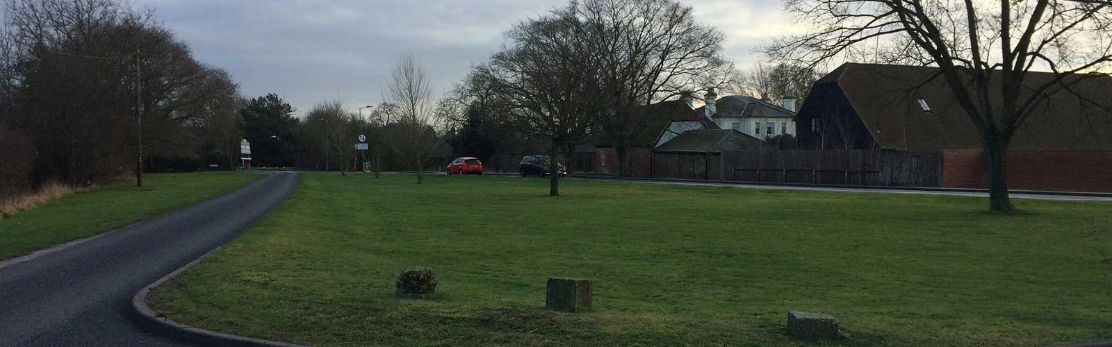 Grass, bare trees and a curving lane beside buildings at Parsonage Green in Broomfield