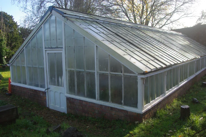A long glass greenhouse on a red-brick base in Blaise Community Garden