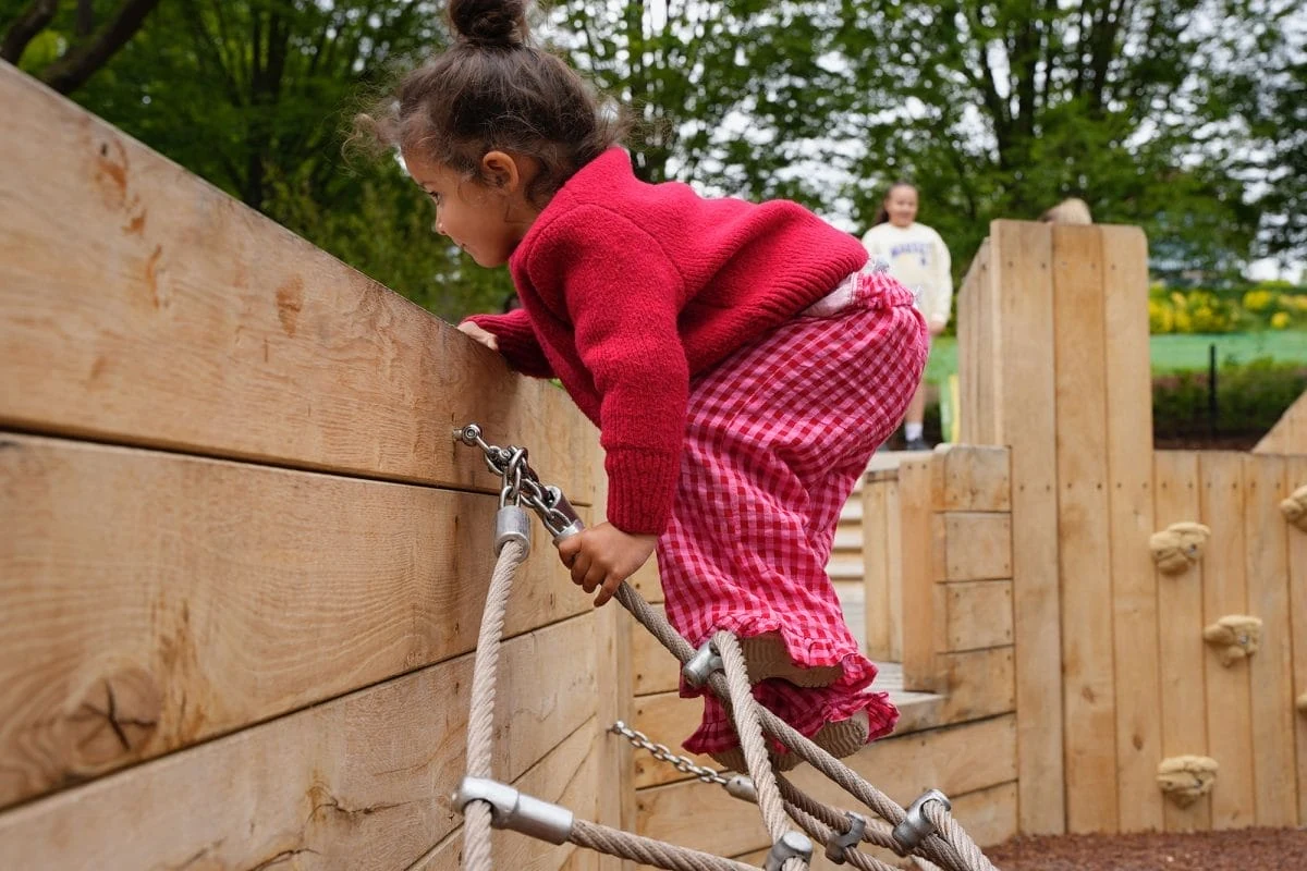 A child in red climbing ropes beside a wooden play structure at the Horniman’s Kusuma Nature Play Area