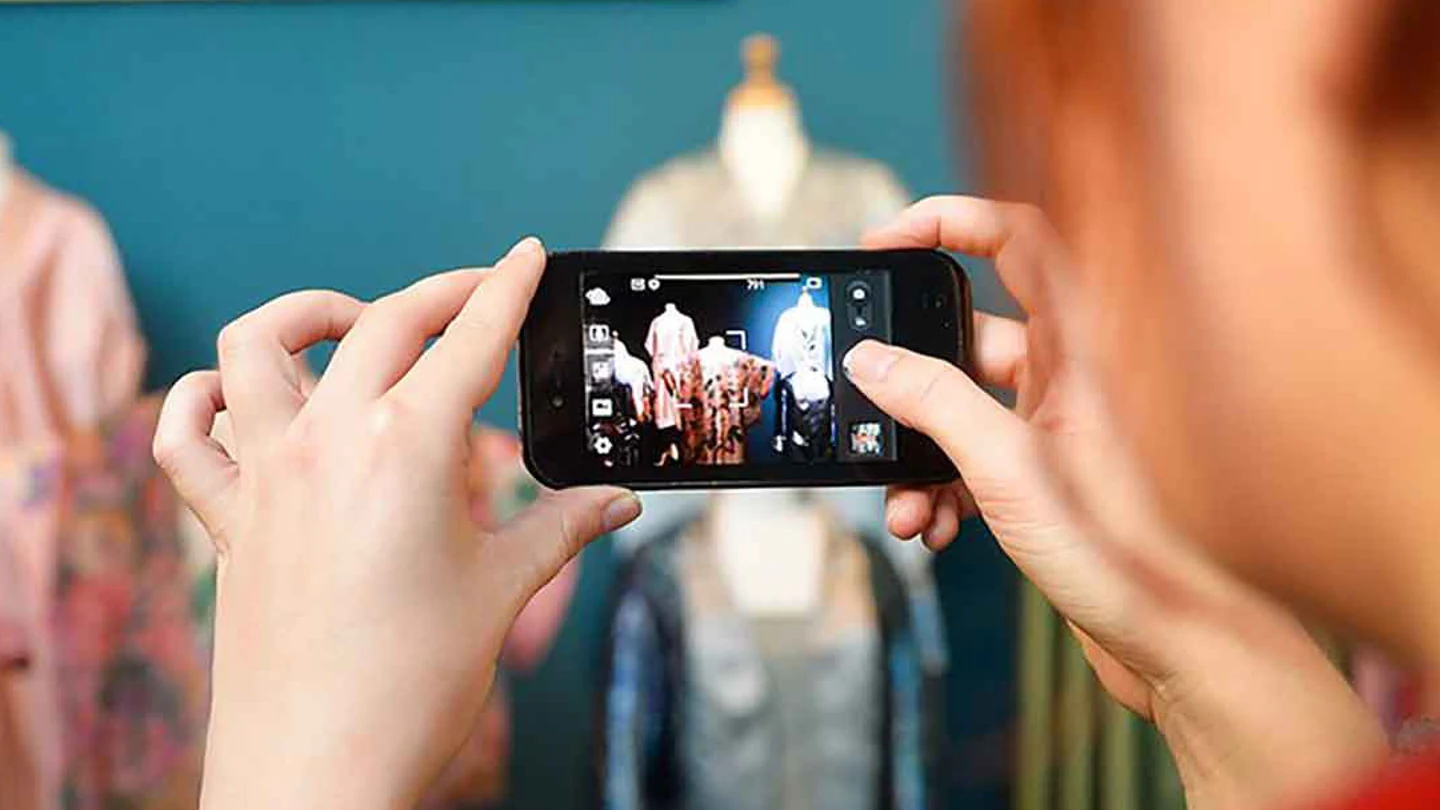 A visitor photographs fashion displays on a phone inside the Fashion and Textile Museum
