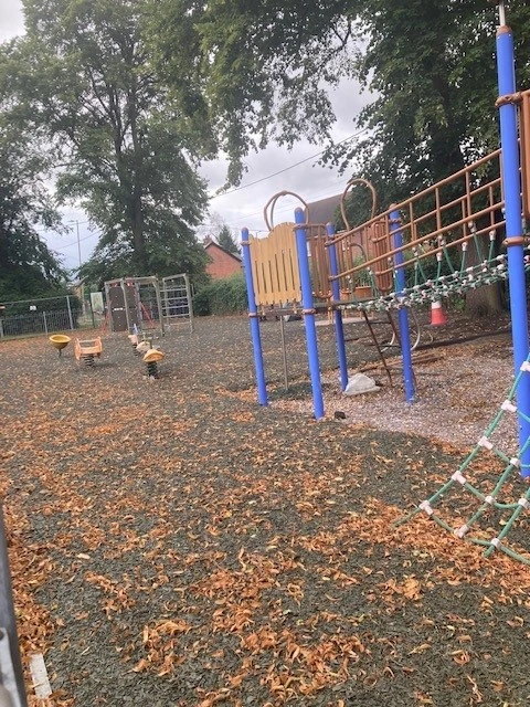 Climbing equipment and rope bridge above a leaf-strewn play surface at Oxney Green Park in Writtle.