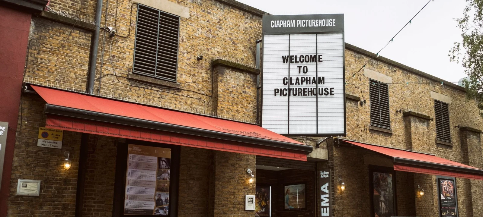 Brick exterior of Clapham Picturehouse with red awnings and its welcome sign
