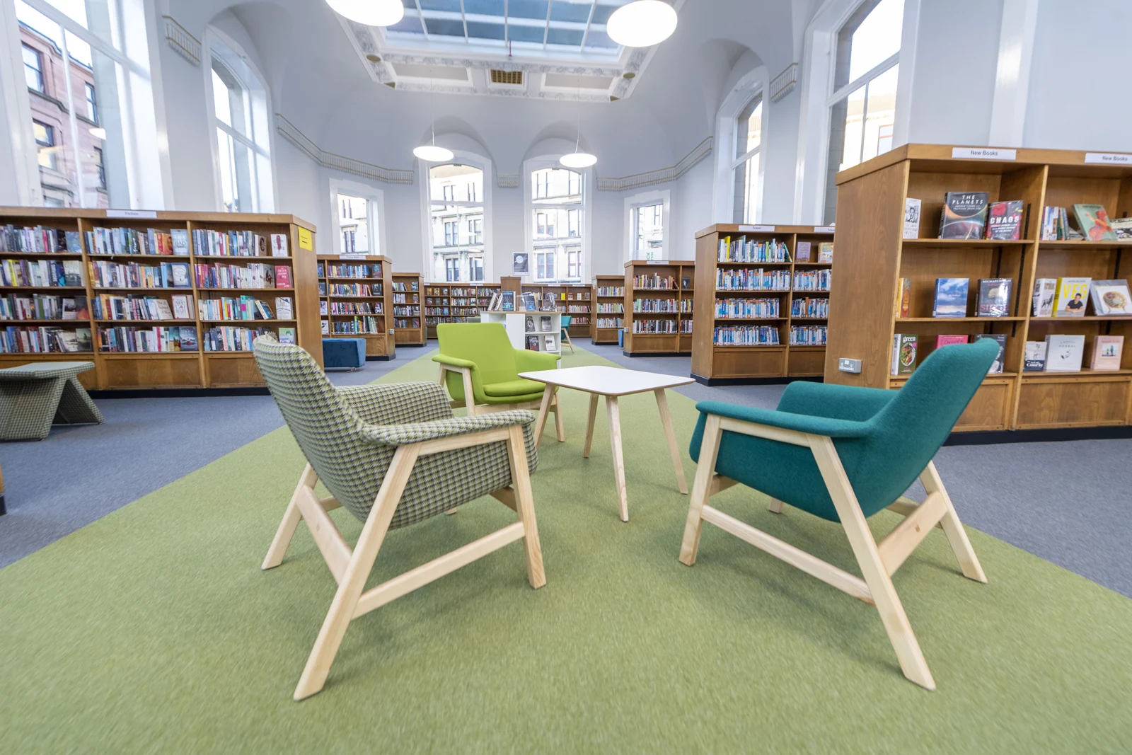 Colourful armchairs around a small table in Partick Library, with bookshelves and tall windows behind