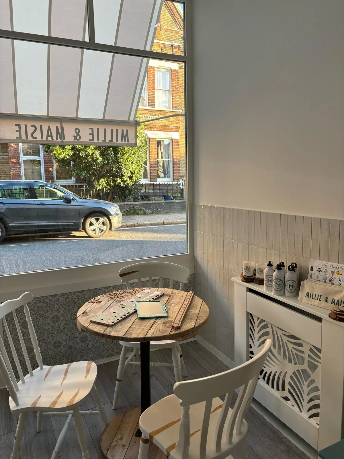 Wooden table and white chairs beside the front window at Millie & Maisie café