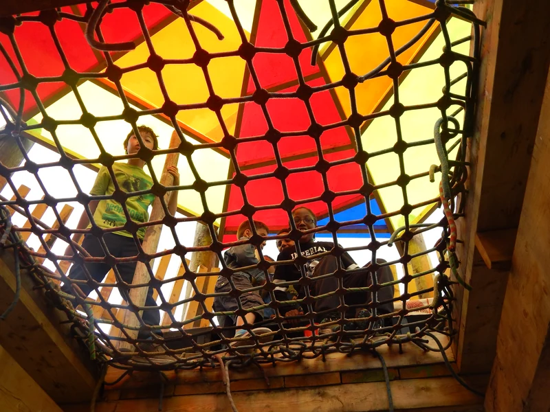 Children looking through a rope play net beneath a colourful canopy at Lollard Street Adventure Playground