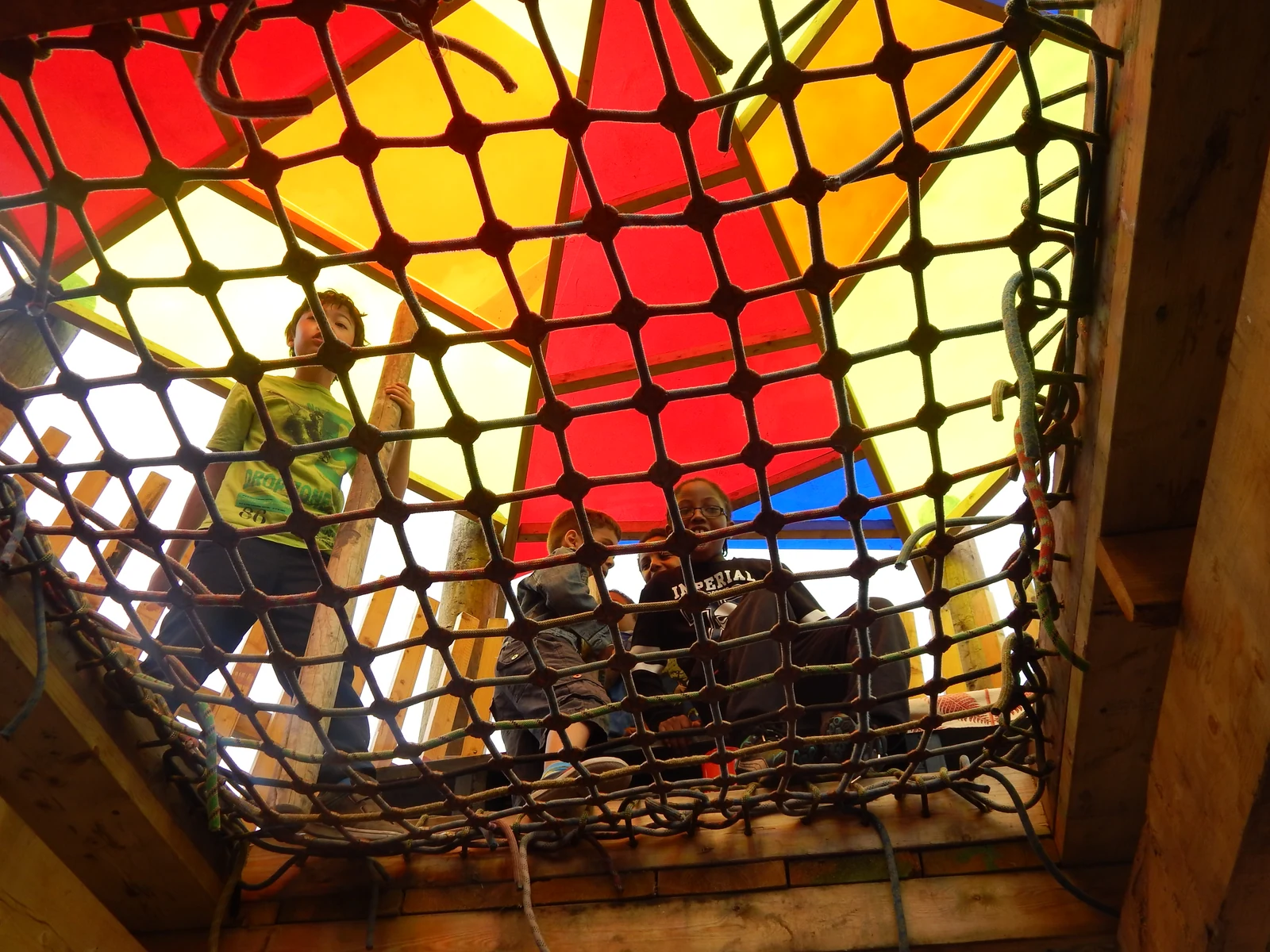 Children looking through a rope play net beneath a colourful canopy at Lollard Street Adventure Playground