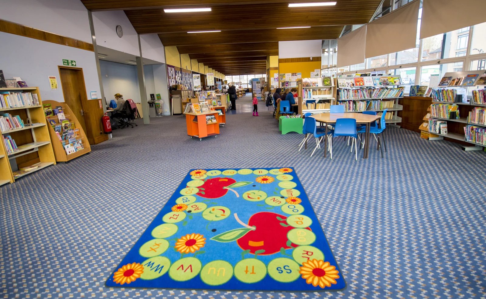 A colourful alphabet rug, blue chairs and book displays in the children’s area of Pollokshaws Library